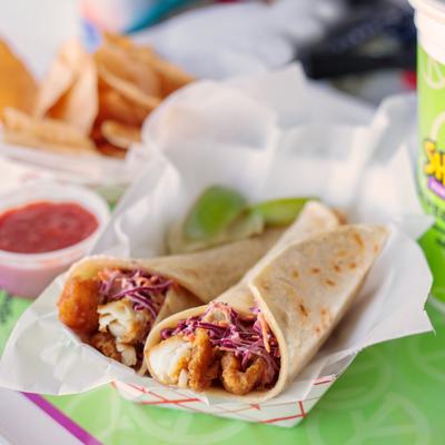 Two fish tacos with special sauce, slaw and lime wedges.