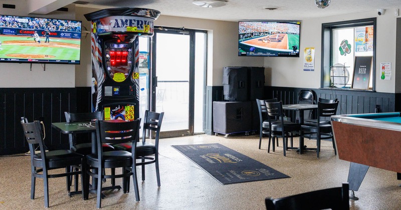 Interior of a sports bar with a TV showing a baseball game, tables, chairs, and a pool table
