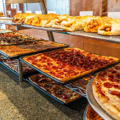 Assorted pizzas and calzones displayed in a glass pizzeria display counter.
