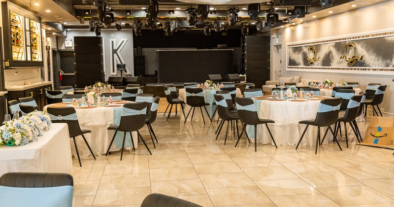 A luxurious and spacious banquet hall with set round dining tables and stylish black chairs