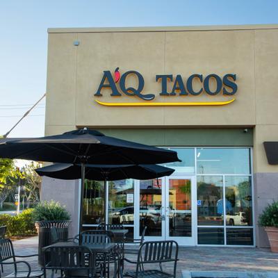 Storefront featuring signage, entrance and outdoor seating under black umbrellas.