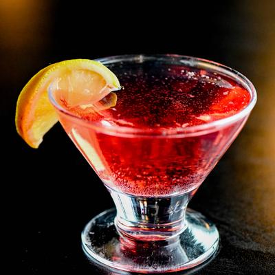Red cosmopolitan garnished with a lemon slice.