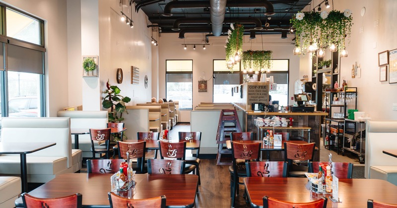 Cozy cafe interior with tables, chairs, booths, and hanging lights with greenery
