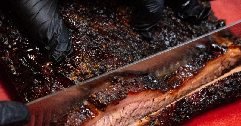 Hands in black gloves slicing smoked brisket