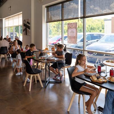 People eat at modern restaurant tables next to large storefront windows.