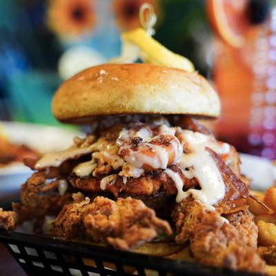 A sandwich topped with shrimp, fried chicken, and bacon, served with fries.