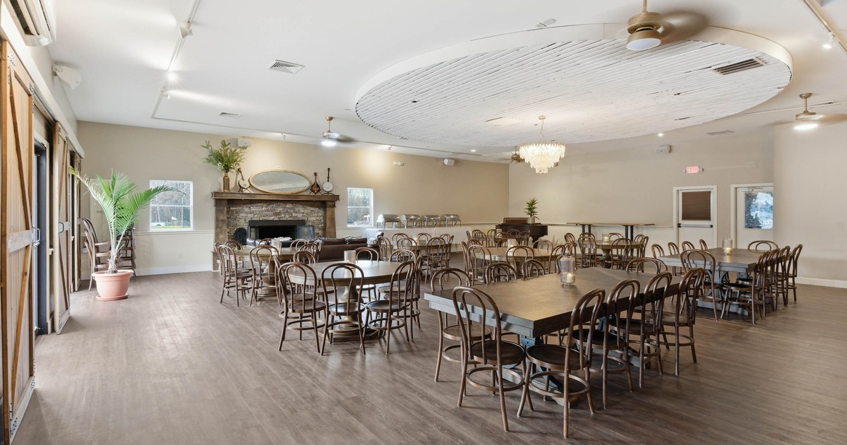 Inside, wooden tables and chairs, a chandelier, and a stone fireplace with a mirror