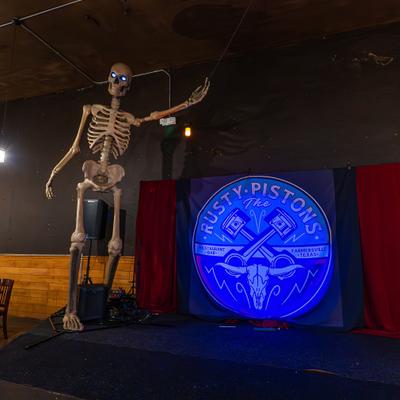 Stage featuring a large skeleton figure and a promotional backdrop with the Rusty Pistons logo.