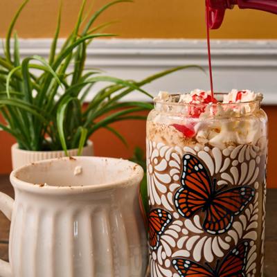 Iced drink in a decorative butterfly jar topped with whipped cream and red syrup.