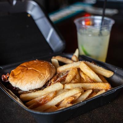 Burger and fries in a takeout container beside a drink in a plastic cup.