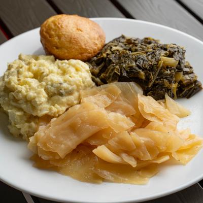 Plate featuring potato salad, sweet cabbage, collard greens, and cornbread.