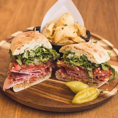 An Italian hero sandwich served with potato chips and two pickled pepperoncini.