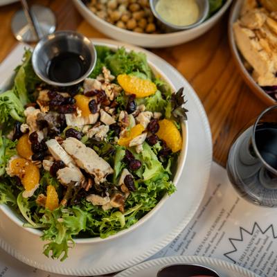 Hideaway signature salad sits on a wooden table surrounded by food and a glass of red wine.