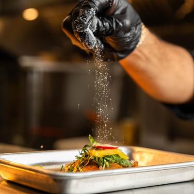 Chef is wearing black gloves while garnishing the meal on a metal tary.