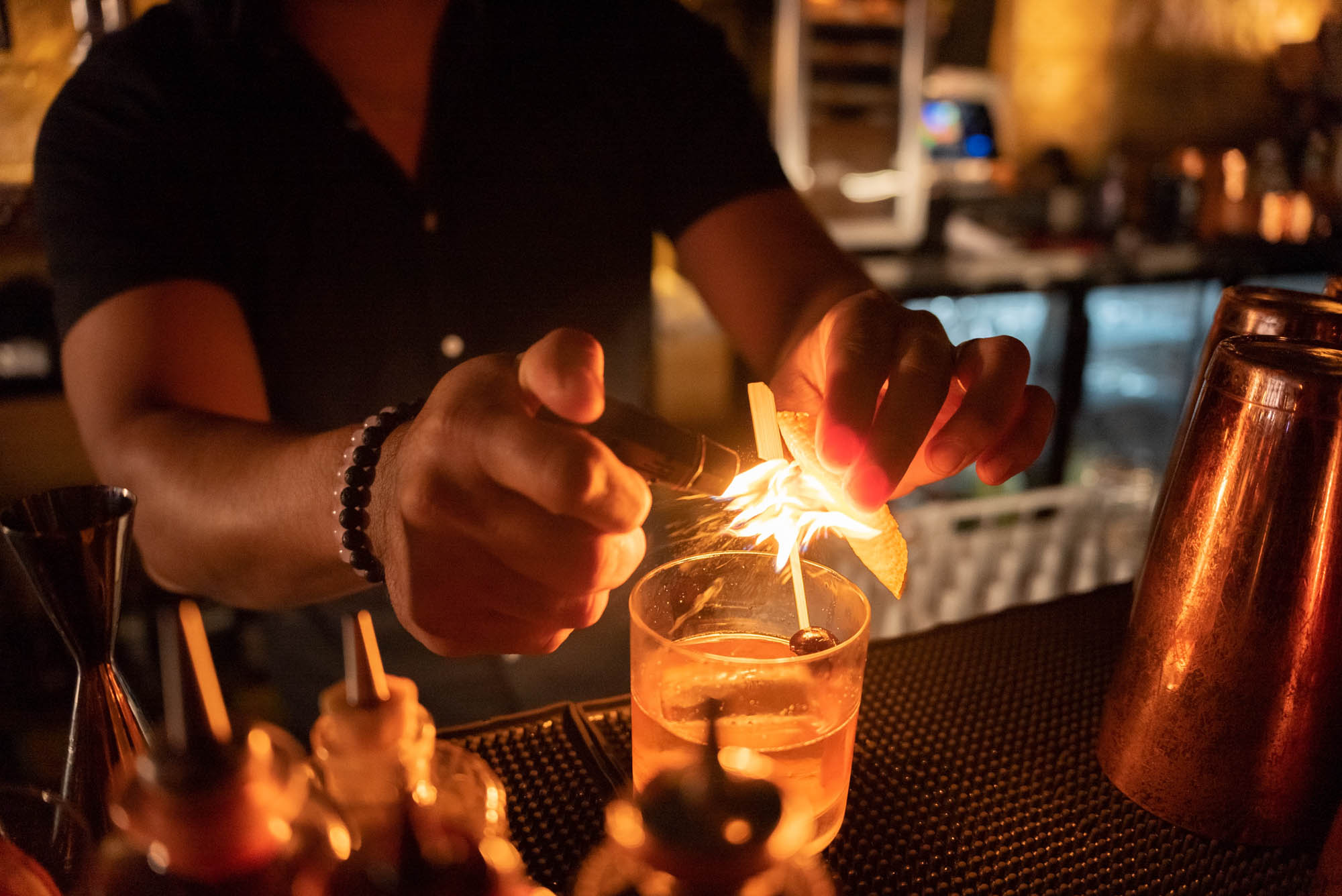 A bartender flaming an orange peel over a whiskey cocktail