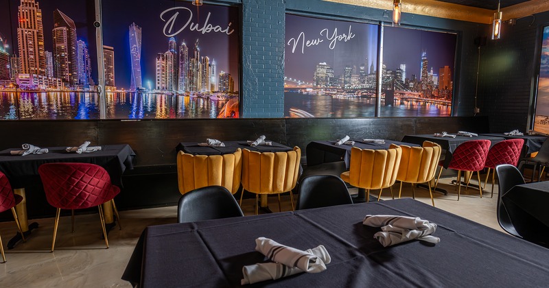 Restaurant interior, lined up tables with black tablecloths, upholstered chairs in different colors