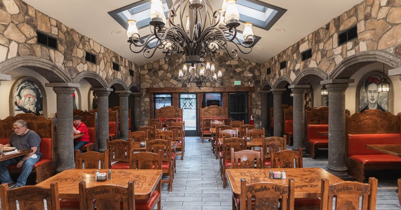 Rustic decor with stone walls, large columns, and a prominent wrought-iron chandelier