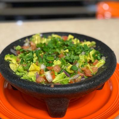 Guacamole in a black stone mortar on an orange plate.