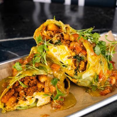 Breakfast burrito topped with a vibrant green sauce and fresh herbs.