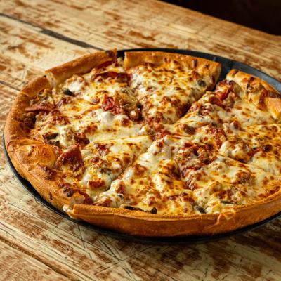 Pizza topped with melted cheese, pepperoni, and sausage, served on a rustic table.