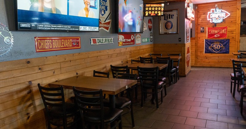 Interior, tables and seats by a wall with large TVs and sticker decorations