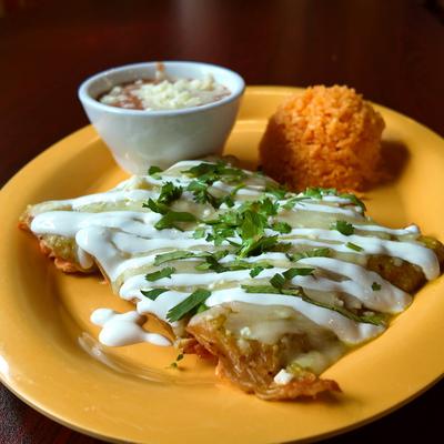 Enchiladas topped with green salsa and sour cream drizzle served with rice and refried beans.