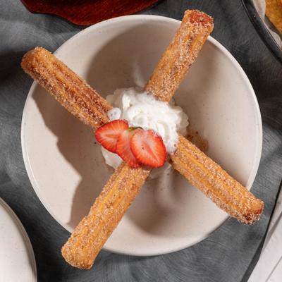 Two cinnamon sugar churros topped with whipped cream and strawberries.