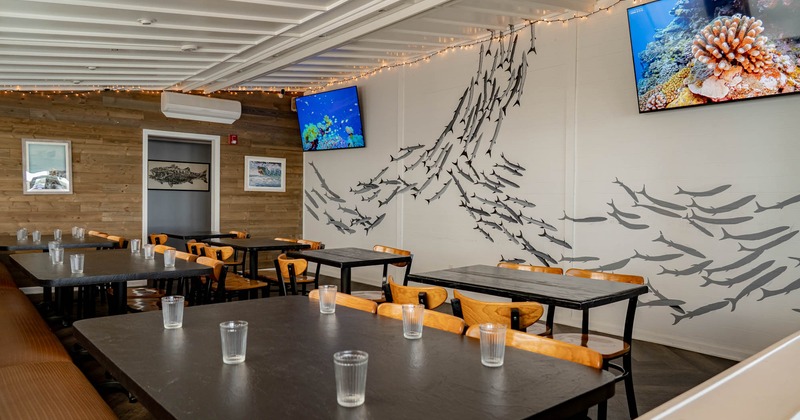 Interior, dining area with nautical decor, featuring tables, chairs, fish-themed artwork, and TVs