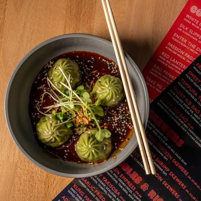 Bowl of veggie dumplings served with chopsticks alongside a menu.