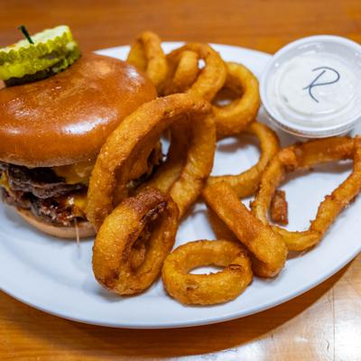 Pitmaster burger served with onion rings and a dipping sauce.