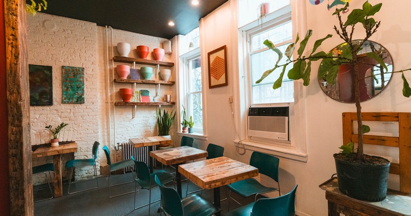 Cozy café with rustic tables, teal chairs, white brick walls, colorful pots on shelves
