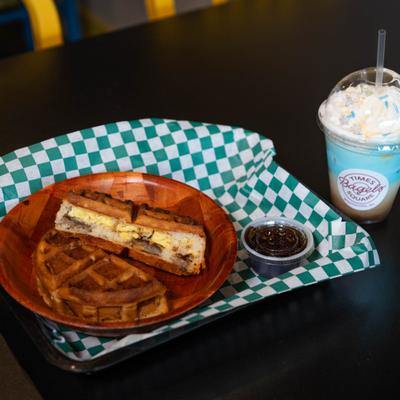 Sausage, egg and cheese stuffed waffle served with syrup, alongside a drink.