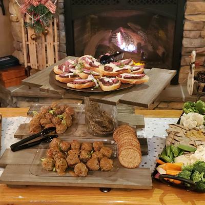 Cozy scene with a rustic table displaying appetizers, a lit fireplace behind.