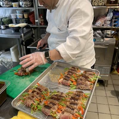 Chef slicing beef rolls with vegetables on a tray in a busy kitchen.