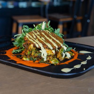 Falafel Cake served over roasted brussels sprouts with arugula and sauces.