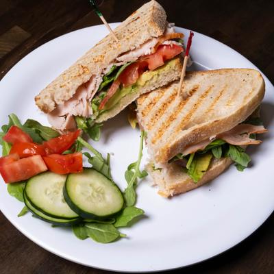 Turkey club sandwich on a grilled bread, served with a small salad.