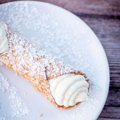 A cannoli filled with creamy ricotta sits on a white plate.