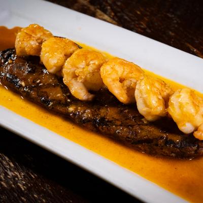 A Surf & Turf dish, featuring a grilled steak topped with prawns and covered in a savory sauce.
