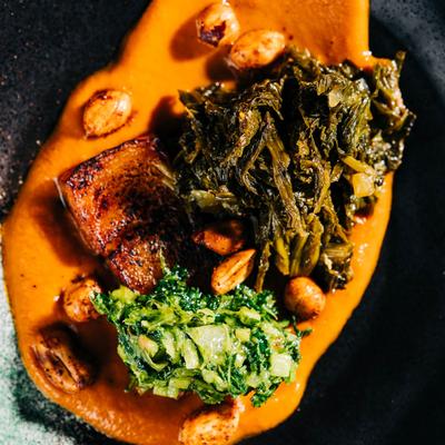 Gourmet dish with seared meat, greens, sauce, and nuts on a plate.