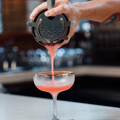 Bartender pouring cocktail in a coupe glass from a shaker