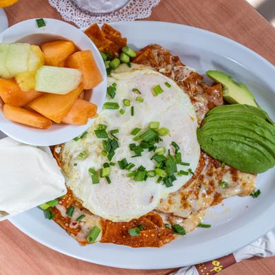 Tortilla chips smothered in salsa, with fried eggs, scallions, cheese sauce, avocado, and fruit.