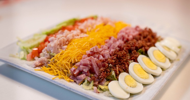 Chopped salad topped with ham, cheese, bacon and eggs