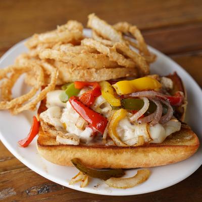 Chicken Cheese steak sandwich with peppers, and onions, served with fried onion rings.