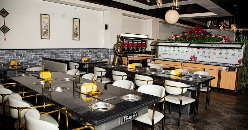 Restaurant interior with hot pot tables, white chairs, decorative lights, and a warrior statue