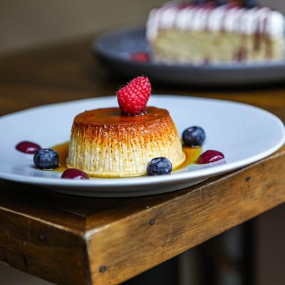A creamy flan topped with a raspberry and surrounded by blueberries.