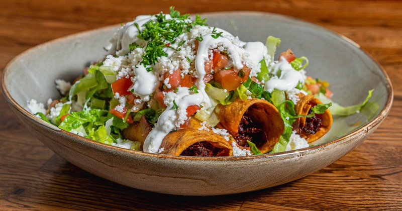 Crispy Chipotle Chicken flautas on a bed of shredded lettuce, guac, and pico de gallo