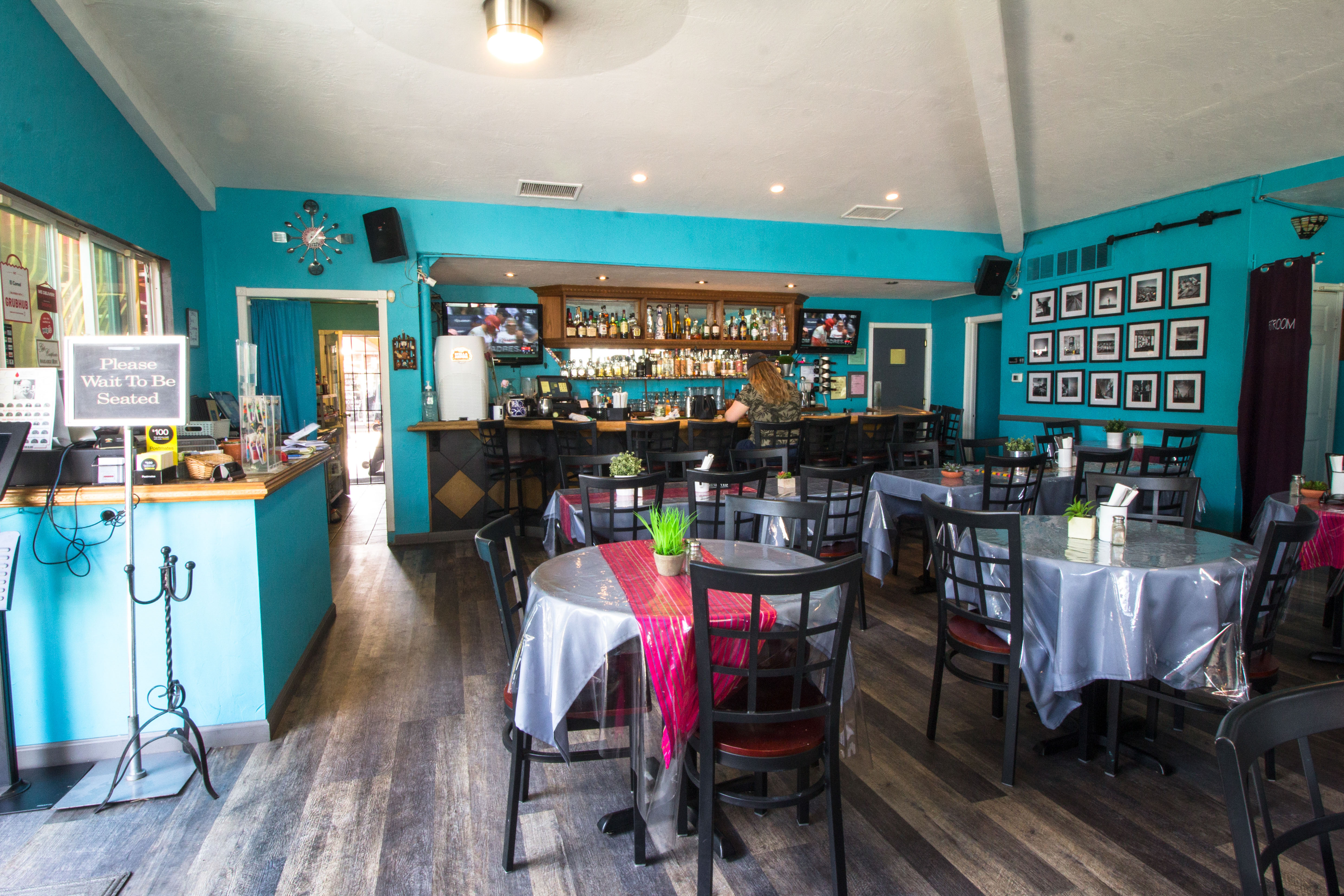 Interior: a prominent blue wall, a wooden bar counter with various bottles, and multiple tables