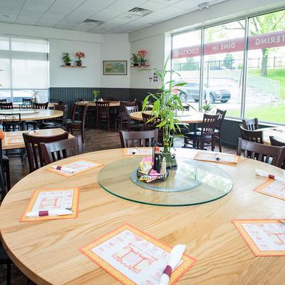 Bright restaurant interior with large round wooden tables, set with placemats and chopsticks.
