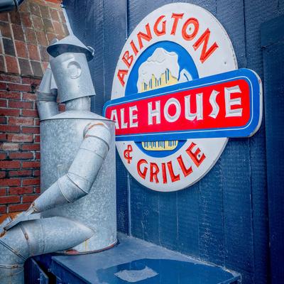 A metal figure sits beside Abington Ale House & Grille logo  sign on an exterior blue wall.