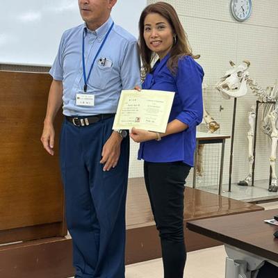 Two people posing with a certificate in a room with a whiteboard and cow skeletal models.
